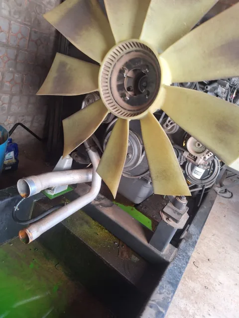 Ventilador amarillo grande del sistema de enfriamiento de generador junto a tubos metálicos.