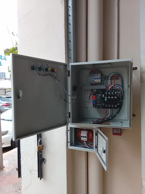 Tablero de transferencia automática abierto con componentes eléctricos y cableado visible, instalado en pared para un sistema de generador.